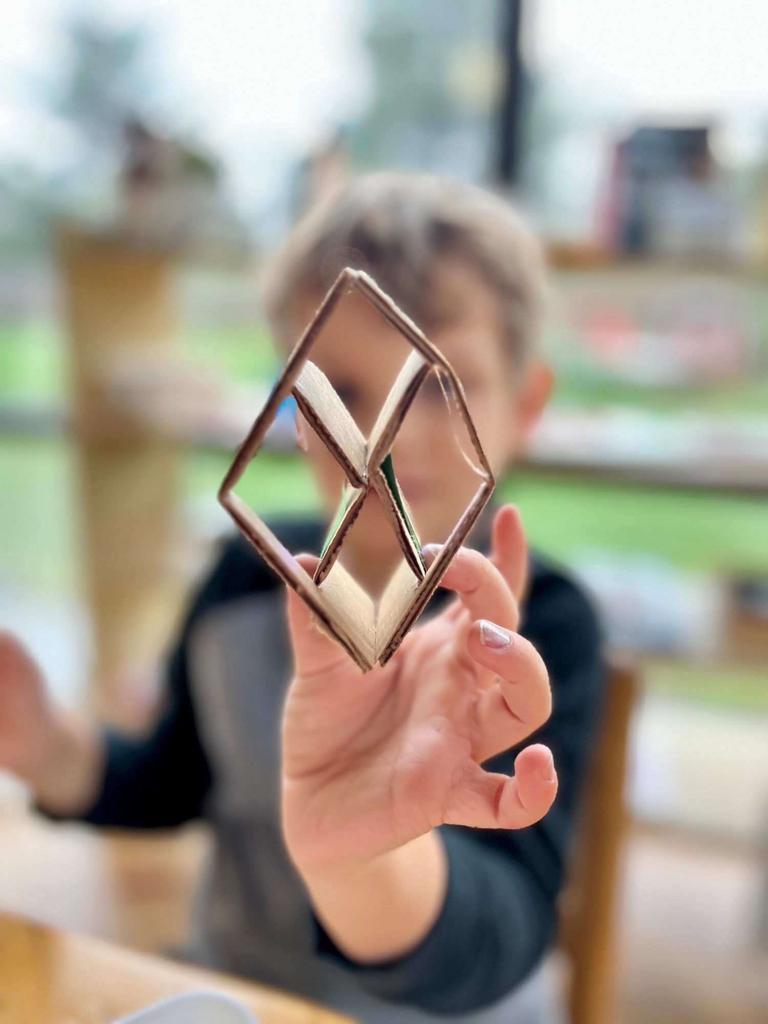 A child holding up a diamond they built from cardboard