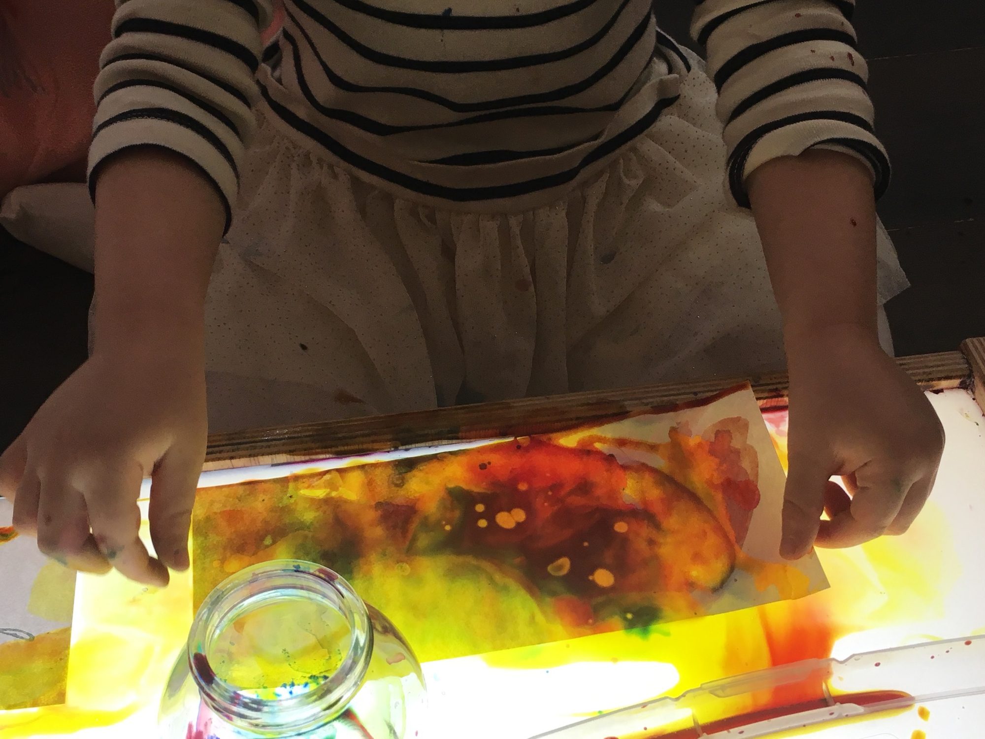 A child moving paint across paper on a light table
