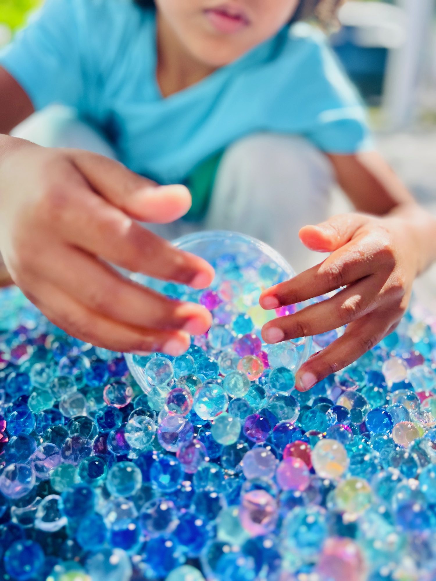 A child running their hands through a tray of water beads